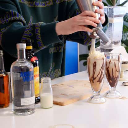 Frozen Espresso Martini cocktails in a milkshake glass being garnished with whipped cream next to a bottle of Absolut Vodka