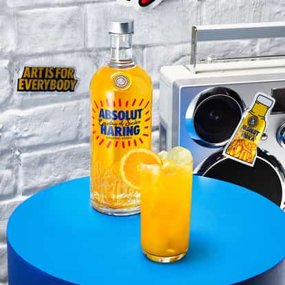 Absolut Haring Screw cocktail garnished with an orange wheel next to a bottle of Absolut Haring and a portable cassette player.