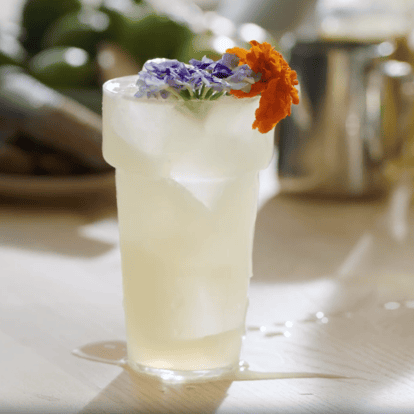 Guilt Tea Pleasure tea cocktail in a highball glass garnished with edible flowers and made with Absolut Lime