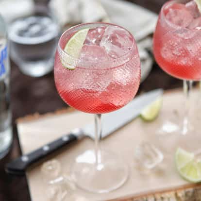 Absolut Moabit served in two balloon glasses with crushed ice and lime wedges on a wooden board.