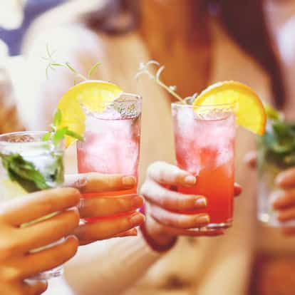 Mocktails iced in tall glasses with orange wedges and herb sprigs