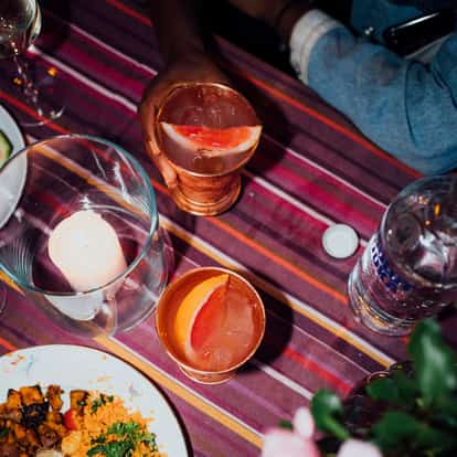 Two mule cocktails in copper mugs garnished with grapefruit wedges, one mug held by a hand on a striped tablecloth.